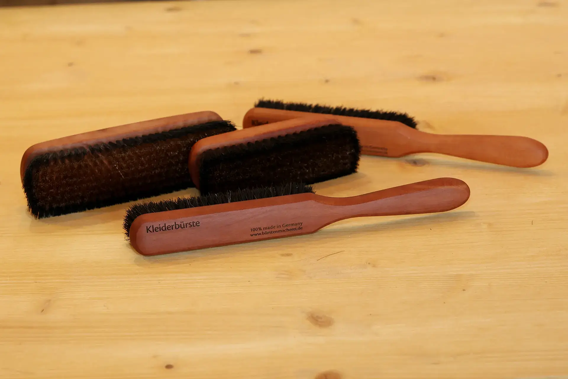 Vier Kleiderbürsten aus Birnbaumholz mit dunklem Naturbesatz, mit und ohne Stiel, eine mit Gravur „Kleiderbürste – 100 % made in Germany – bürstenmacherei.de